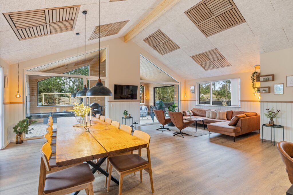 Åben stue og spisestue med sofaer, lænestole og stort spisebord set i fugleperspektiv