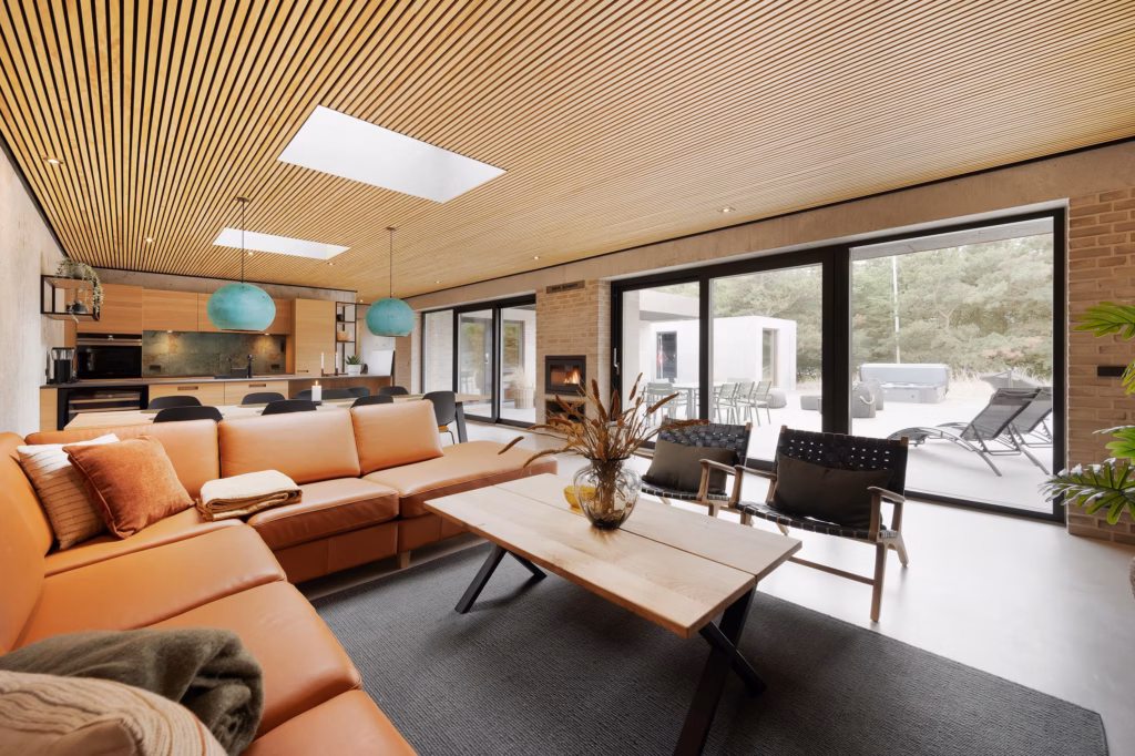 Bred stuevinkel med cognacfarvet lædersofa, loungestole og sofabord med udsigt til terrassedøre i sommerhus i Bjerregård