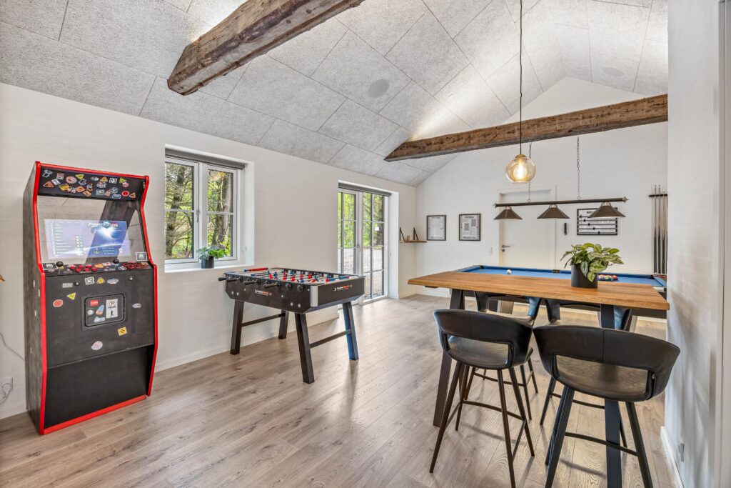 Arcade-skab, bordfodbold og højbord med barstole i spilleværelse