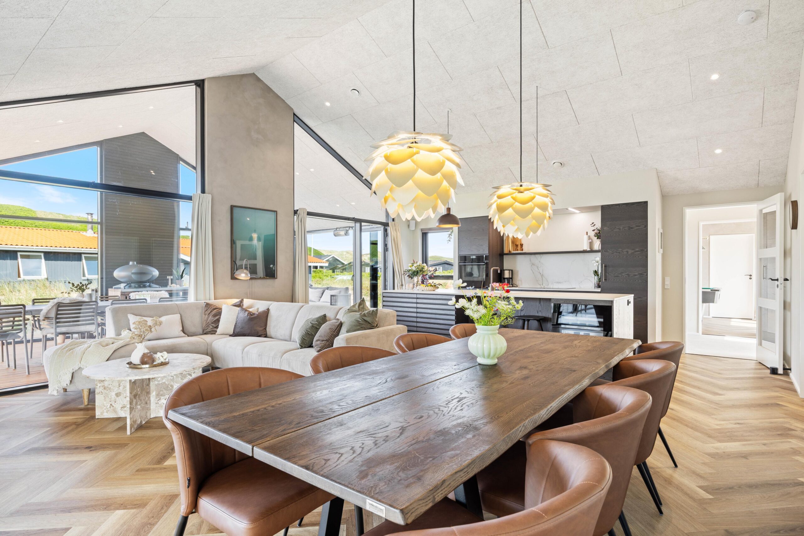 Åbent opholds- og spiseområde møbleret med sofa, spisebord og stole under højt loft