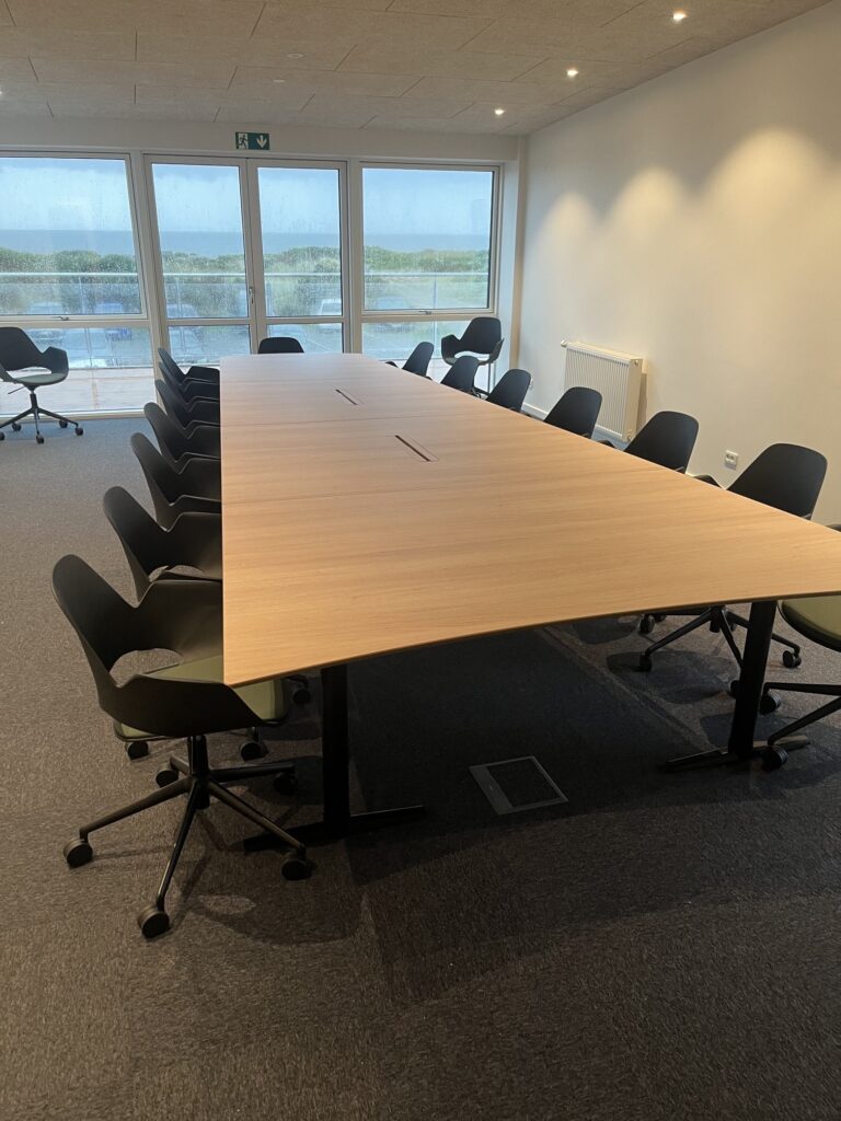 Langt konferencebord med stole på hjul foran det store vinduesparti